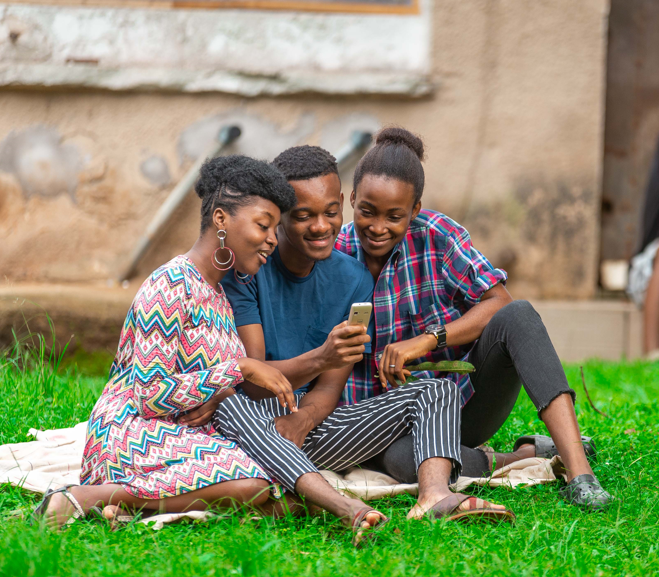 Three people sharing a mobile phone outdoors